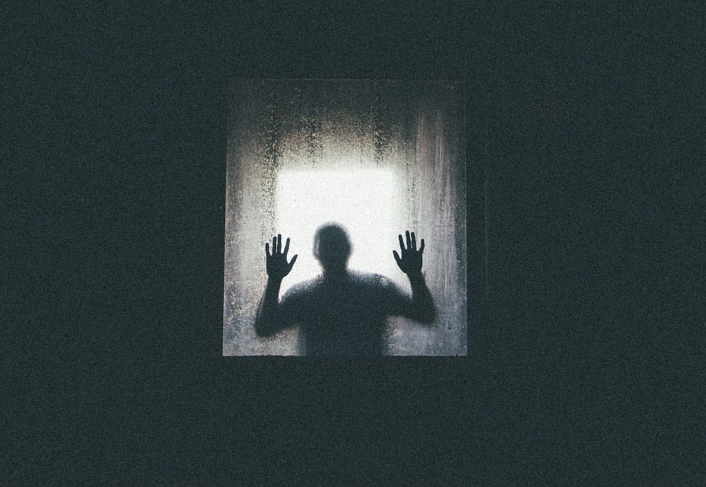  A dark figure with hands pressed against a frosted glass window with a bright light behind it, representing dreams about ghosts in different cultures.